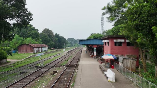 Rural Railway Station Platform with Parallel Train Tracks Surrounded by Green Trees under Cloudy Sky