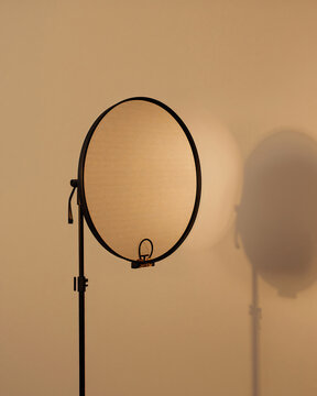 Circular reflector on a black metal stand casting a soft shadow against a plain beige wall in a studio lighting environment