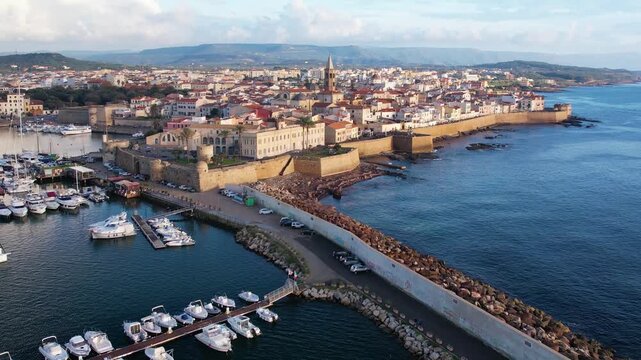 Aerial view of Alghero, Sardinia, showcasing its vibrant coastal scenery, historic buildings, and tranquil waters. Ideal for travel enthusiasts and explorers at sunset.