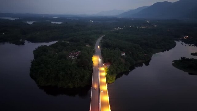 Aerial view captures a glowing bridge spanning dark water at dusk at Tasik Raban