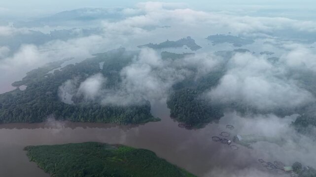 Aerial view of a misty river flowing through lush green islands. Clouds drift over dense forests at Tasik Raban