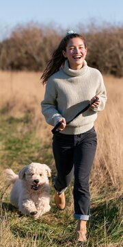 Young woman jogging with dog along grassy path for lifestyle poster and outdoor background