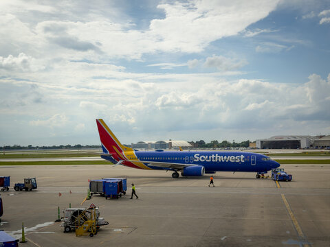 LOUISVILLE, KY, JUN 9, 2026: Full side profile of Southwest Boeing 737 being towed, with a worker walking past baggage carts and a fueling cart, hangar and cloudy sky behind
