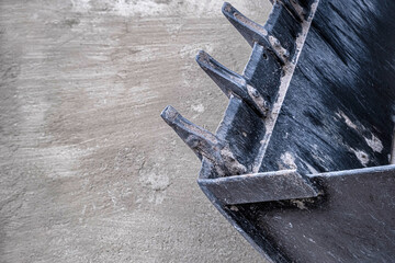 Excavator bucket teeth on concrete. Close-up of a worn steel digging bucket with mud-caked cutting teeth resting on a concrete surface. Useful for construction, mining, or heavy industry content. © ismailgazel