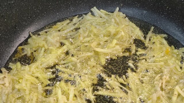 Large grated potato fritter cooking in a frying pan. Hot oil bubbles around the potato pancake as a golden crispy crust forms during frying. Homemade potato pancake made from coarsely grated potatoes.