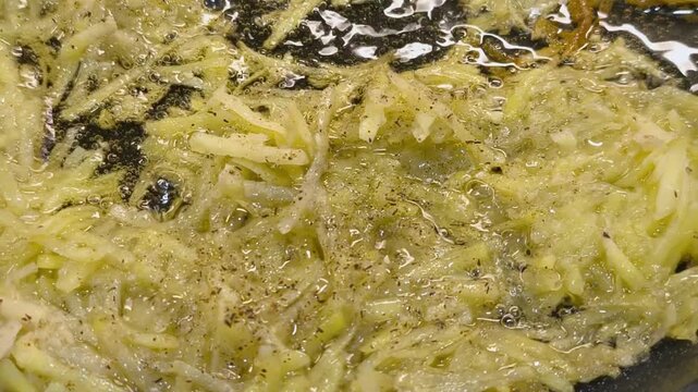 Large grated potato fritter cooking in a frying pan. Hot oil bubbles around the potato pancake as a golden crispy crust forms during frying. Homemade potato pancake made from coarsely grated potatoes.