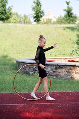 Stylishly dressed girl practicing rhythmic gymnastics while handling a hoop on an outdoor track.  Young Girl Practicing Rhythmic Gymnastics Outside with a Hoop © Loginova