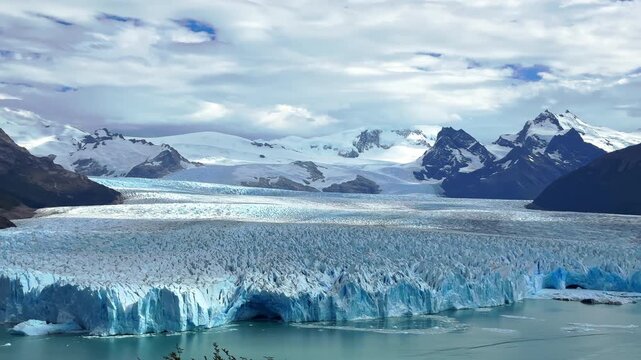Scenic aerial drone footage of the magnificent Perito Moreno Glacier in Argentina, showcasing majestic ice formations, snowy mountains, and tranquil turquoise water under a dramati