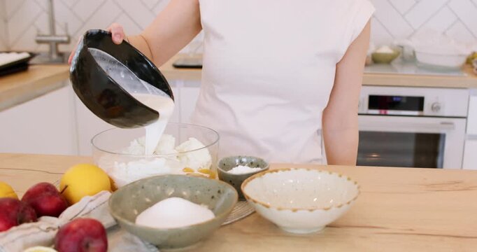 Homemade recipe. Pastry cooking. Female chef pouring liquid cream in glass bowl with cottage cheese eggs on table with fresh fruit.