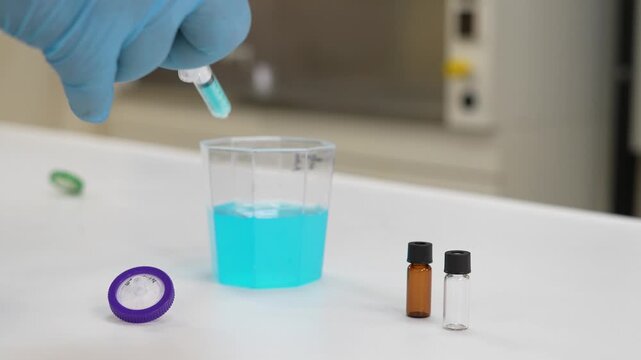 Lab technician filtering blue solution through syringe filter into sample vials, pharmaceutical research