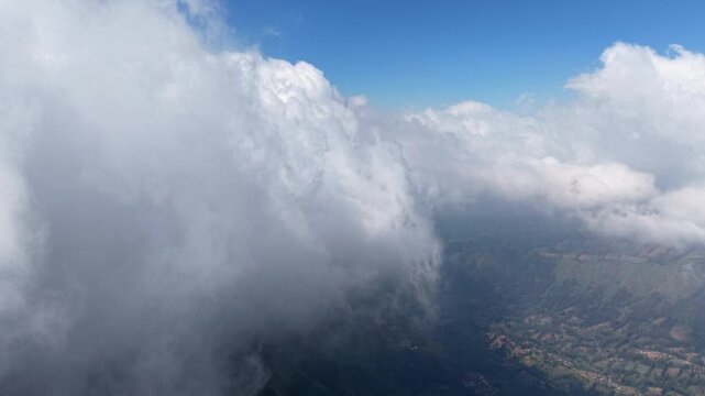 Massive clouds drift above mountainous terrain. Below, green valleys stretch under bright blue skies at Wonokerto