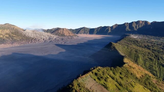 Aerial view of vast volcanic crater at dawn. Sunlight glints on rugged, rocky terrain near Bromo