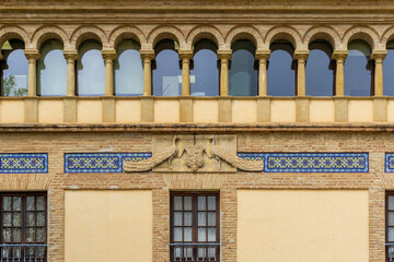 Ornate building facade featuring traditional Moorish-style arches, historic brickwork, colorful ceramic tile patterns, and a sculptural peacock heraldry motif in Córdoba © photoopus