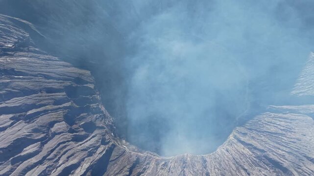 Steam rises from volcanic Bromo crater. Rugged terrain surrounds the opening