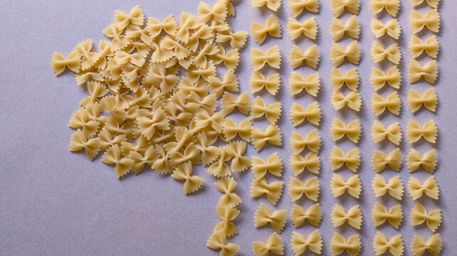 Raw farfalle bowtie pasta arranged in neat columns and disorganized pile on grey background top view