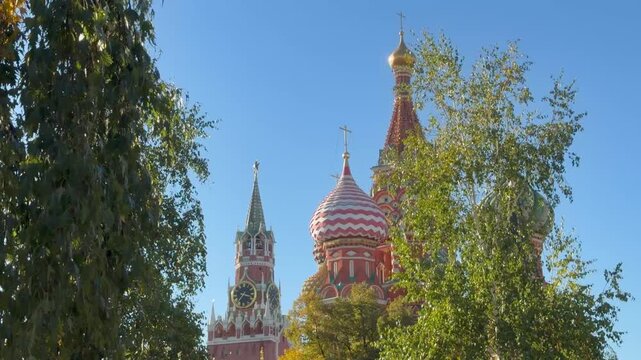 Scenic view of Saint Basil Cathedral and Spasskaya tower of Moscow Kremlin framed by green birch tree branches against blue sky, Russia. Red Square, landmark cathedral, historic tower, autumn season.