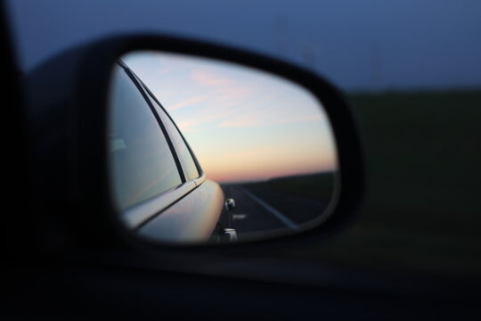 Car side mirror view with road and sunset sky, road trip and travel concept