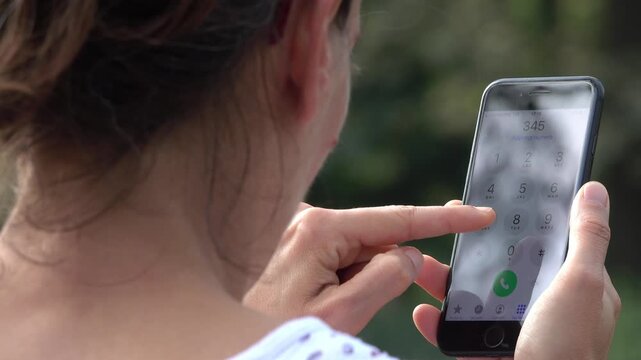 Woman using a smartphone to make a call pressing the screen to initiate a phone conversation during a quiet moment in the garden