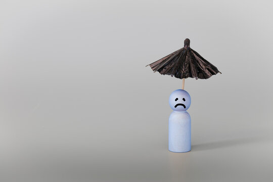 Psychology, solitude, fear or mental health problem concept. Depressed sad person with a cloud overhead, on grey background. Wooden figure with black umbrella symbolize mental health.