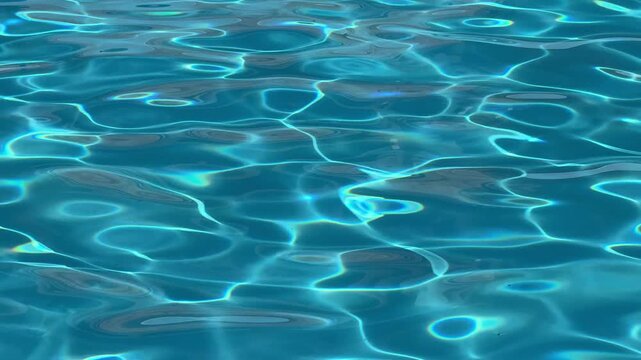 Refreshing background of crystal clear blue water surface with sunlit ripples and caustic patterns in a swimming pool