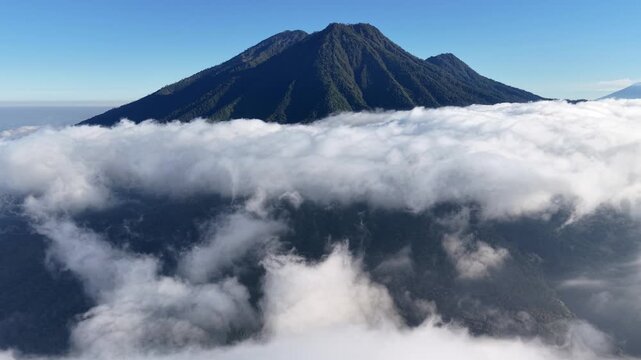 Low perspective of Mount Kawi towering above a sea of clouds under clear blue sky.
