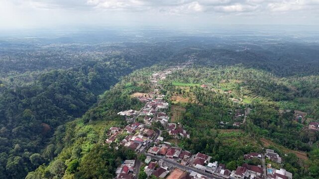 High altitude drone panorama of Wonosari village, tropical hills, forests and agricultural terraces under hazy sky.