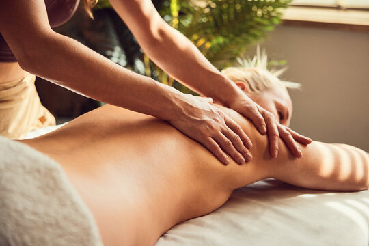Therapist giving back massage to woman in sunlit spa