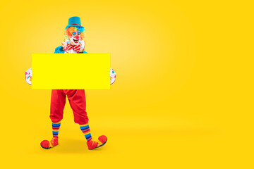 Funny clown holding sign blank template mock up for advertising, posters, greetings, invitations. Entertainer as Joker in a suit and wig, with clown whiteface makeup © TSViPhoto