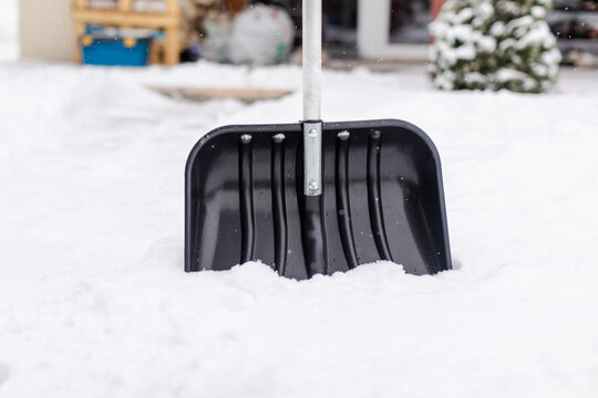 Snow-covered yard with upright shovel ready for clearing during quiet and snowy winter day, closeup