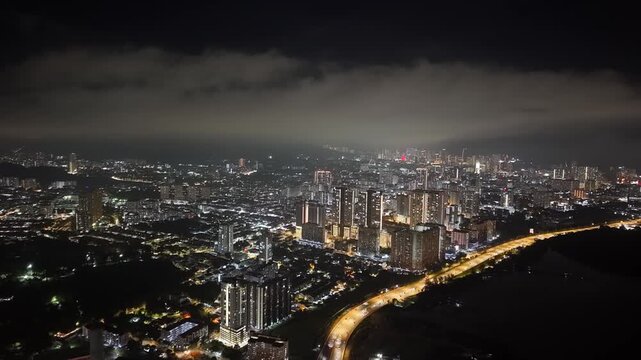 City lights glow under dark, cloudy night sky. Urban sprawl stretches wide at Jelutong, Penang