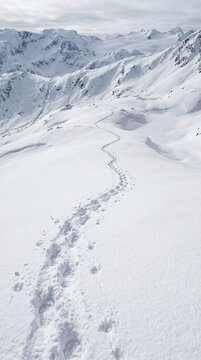 Footprints on Snowy Mountain Trail Path in Winter Landscape with Majestic Peaks