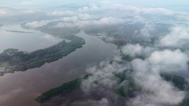 Aerial landscape showing a winding river flowing through green islands and surrounded by misty clouds under a calm and serene sky at Tasik Raban
