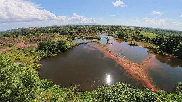 Wide fisheye aerial view of interconnected marsh lakes, red sediment shores and dense tropical vegetation under blue sky