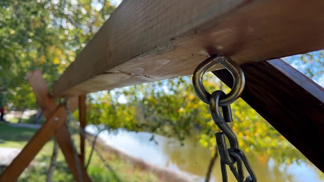 Close up of metal chain and eye bolt attached to a wooden beam of a swing set in a park