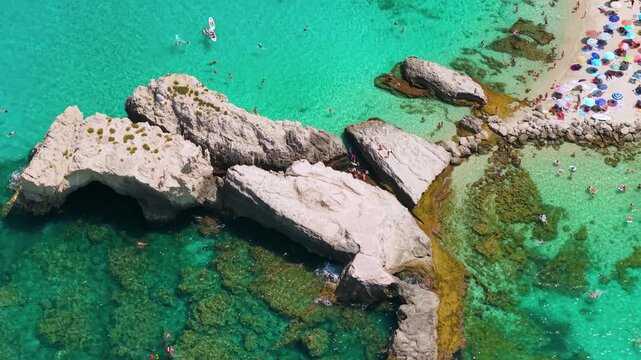 Baia di Riaci Tropea Calabria Italy 4k drone view of iconic rock reef beach. Speedboat tracking shot towing water tube inflatables, tilt up reveal of white cliffs and distant Tropea broll video