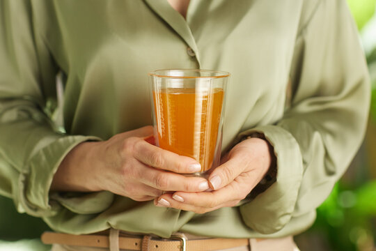 A close-up view of a woman holding a refreshing glass of orange juice, symbolizing hydration, nutrition, and a healthy morning wellness routine in a serene setting.