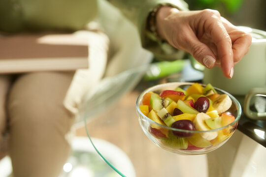 A close-up shot of a hand reaching for a bowl of fresh fruit salad on a glass table, highlighting healthy food choices and wellness during a relaxing break at home.
