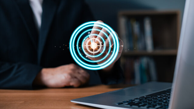 Businessman touching a glowing virtual dartboard to achieve corporate mission and target goals. Professional working on laptop computer, aiming for business marketing strategy and success.