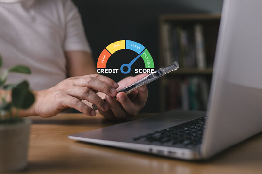 Man holding smartphone with excellent credit score speedometer icon on screen while working on laptop. Personal finance, loan approval, banking rating, and debt management concept at desk.