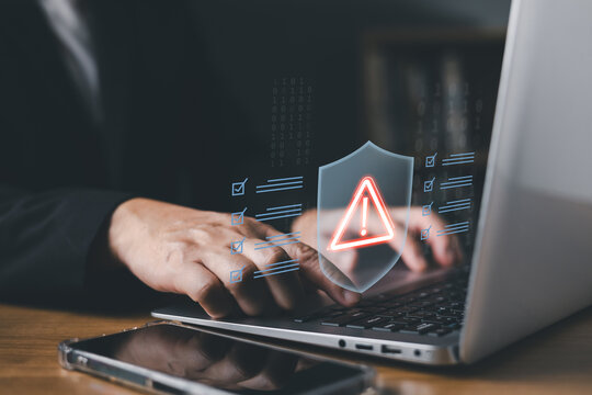 Cybersecurity warning and error alert concept. Businessman using laptop with glowing shield triangle warning sign to protect network data against cyber threats and security bugs in office.