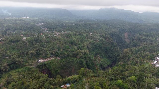 Clouds linger over dense, green mountain valleys. Paths wind between trees at Tumpak Sewu