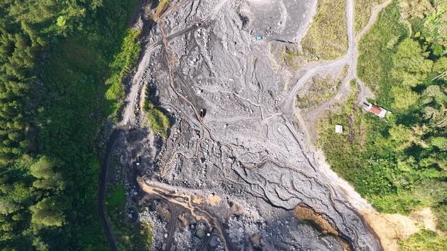 Aerial drone view of a dark, dried volcanic lava trail winding down the steep, rugged slopes of Mount Semeru.