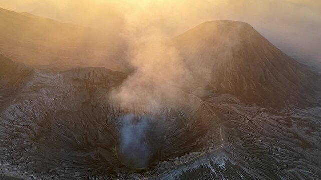 Golden light bathes a smoking volcano Mount Bromo. Steam rises from the crater dark mouth