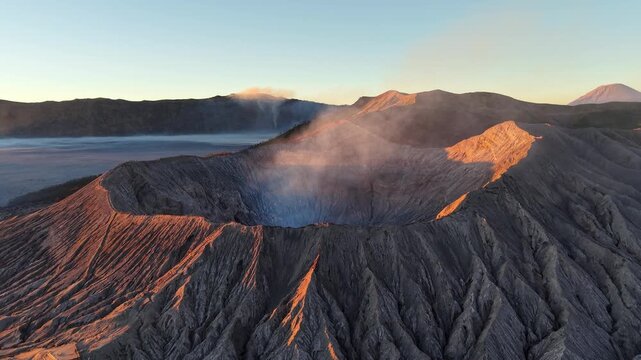 Sunrise bathes volcanic Bromo crater in warm light. Steam rises from active crater