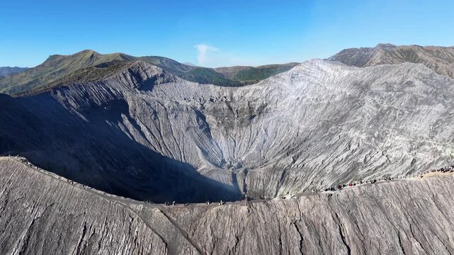 Dramatic sunrise lit volcanic crater rim with hikers, steam vents, ridged ash walls and surrounding green mountains near Bromo