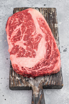 Raw marbled beef rib eye steak entrecote cut on rustic wooden board. Fresh premium butcher meat with rich fat marbling and copy space.