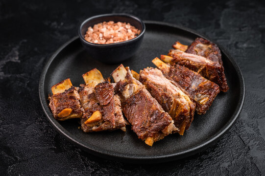 Roasted lamb ribs slab cut into portions with rich texture on dark stone background food photography