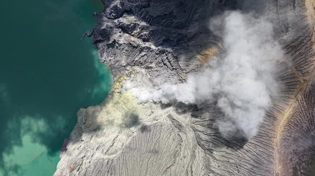 Birdseye drone shot of Mount Ijen crater lake showing sulfur vents and turquoise acidic water.