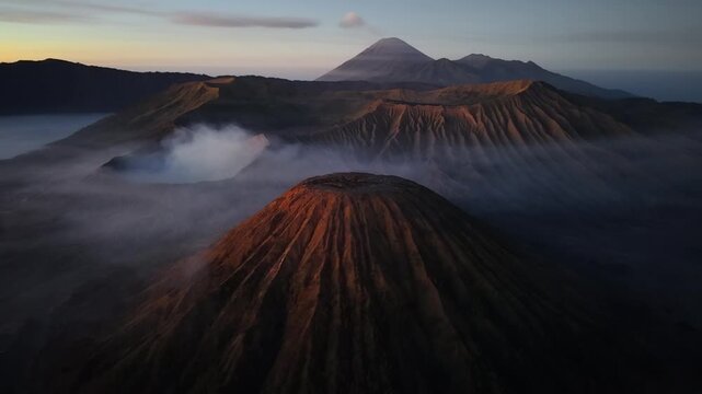 Misty dawn wraps volcanic peaks in soft, drifting clouds. Golden light touches ridges, casting warm at Bromo