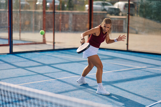 Female player hitting ball with racket during paddle tennis match on court.